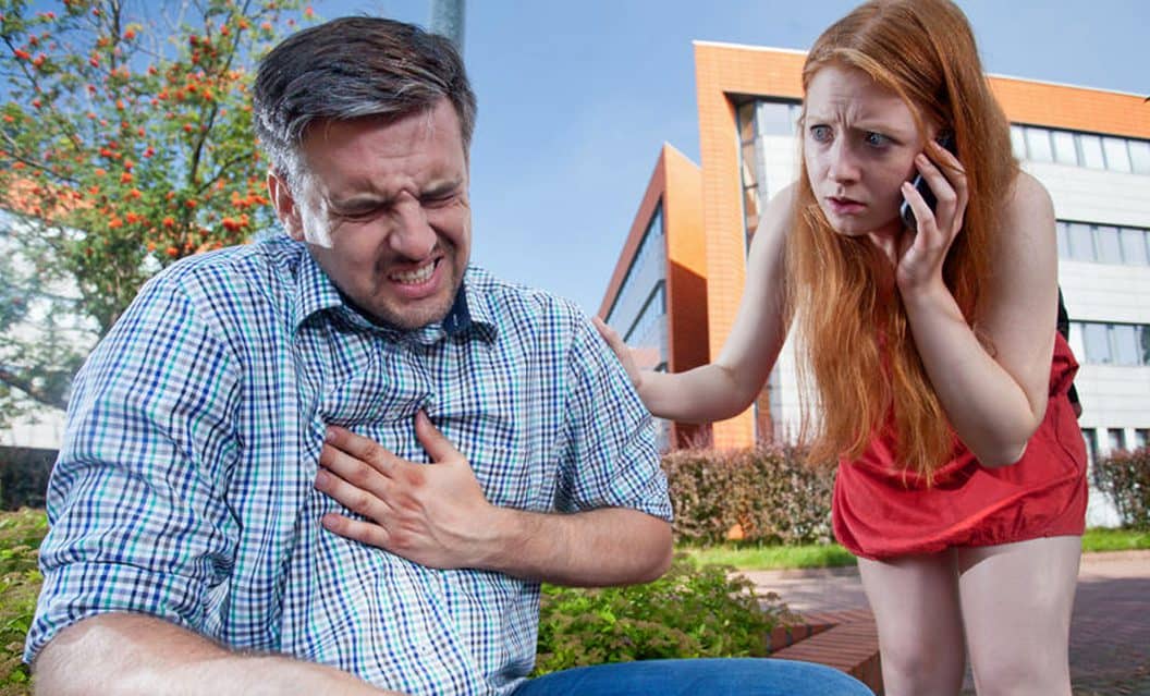 אדם מחזיק את חזהו ונראה סובל מכאבים בחזה ולידו אישה מודאגת המתקשרת לרופא בעקבות הלחץ בחזה של האיש לידה